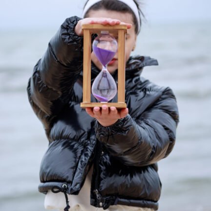 Young female holding sand clock at the beach. High quality photo