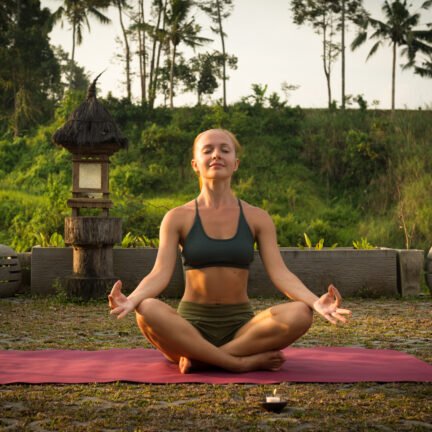 Young woman meditating in lotus posture at sunset with candles